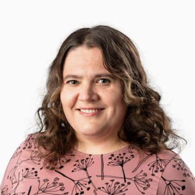 Elina Wallinin kasvokuva. Hänellä on kiharat ruskeat hiukset, leveä hymy ja roosanvärinen kuviollinen paita.