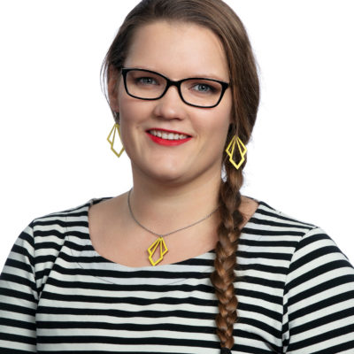 Laura Lindholm on pukeutunut mustavalkoraidalliseen paitaan, hänellä on silmälasit, pitkät ruskeat hiukset letillä ja keltainen kaulakoru ja korvakorut.