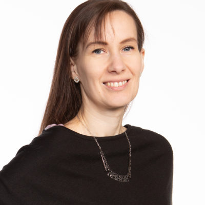 Sabriina Heikkilä katsoo hymyillen kameraan. Hänellä on ruskeat pitkät hiukset, musta paita ja korvakorut ja kaulakoru.